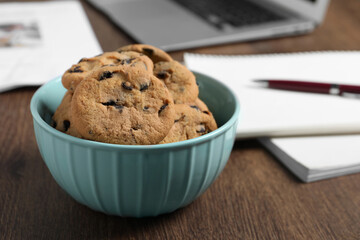 Bowl with chocolate chip cookies on wooden table in office, closeup