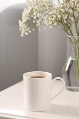 Fototapeta na wymiar Ceramic mug with tea on white bedside table indoors. Mockup for design