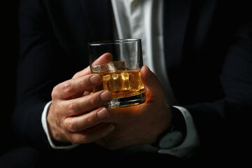 Man holding glass of whiskey with ice cubes on black background, closeup