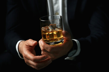 Man holding glass of whiskey with ice cubes on black background, closeup