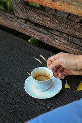 Hand hold white coffee cup on wooden table with autumn leaves. Outdoor lifestyle. Refreshment summer drink with copy space. 