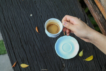 Hand hold white coffee cup on wooden table with autumn leaves. Outdoor lifestyle. Refreshment summer drink with copy space. 