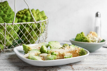 Plate with cut romanesco cabbage on light wooden table