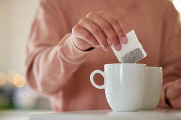 Ending my day with a hot cup of tea. a woman dropping a tea bag into a waiting mug.