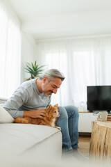 Smiling Mature adult man sitting on couch playing with chihuahua dog, Lifestyle concept, Middle aged male enjoying with pet in living room at home.