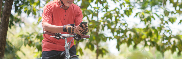 Close up Asian Senior man Hands using mobile phone or smartphone for online application while travel with bicycle outdoors. Searching GPS coordinates. Grandfather exercising with bike riding. 