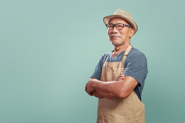Portrait of Asian Senior man wearing brown apron smiling with arms crossed over isolated color...
