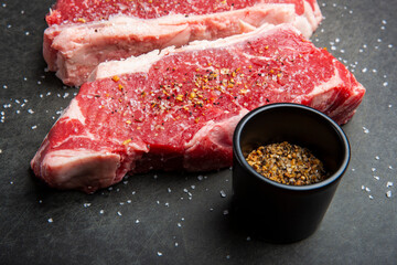 Close up of raw strip loin steaks on black cutting board with salt and spices.