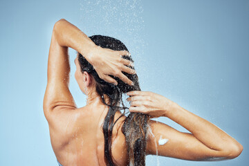 Rinsing all the shampoo out of her hair. Studio shot of an attractive young woman washing her hair while taking a shower against a blue background.
