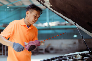 Senior Asian man checking or measuring a vehicle oil engine or engine lubricant level by using oil...