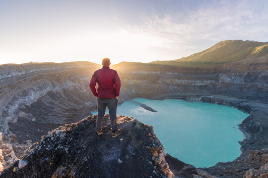 Mountaineer man looking at the Poas Volcano Crater Lagoon at sunrise surrounded by volcanic rocks in the Poas Volcano National Park in the Alajuela province of Costa Rica