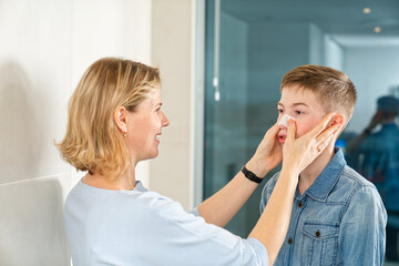 mom glues a patch to remove blackheads to her son. acne remover patch. teenage with nose band aid