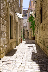 Fototapeta na wymiar Narrow street with stone houses. Old houses and old narrow alley in Trogir, Croatia, Europe. Streets in old town.