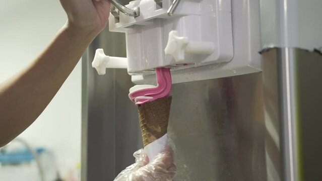 Demonstration View Of A Crew Pouring Strawberry-Vanilla Ice Cream On A Waffle Cone Usinf Ice Cream Machine. static