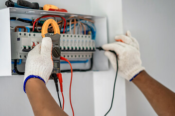 An electrical engineer is working on a home electrical control panel system and checking the current with a voltmeter.