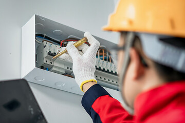 Asian electrical engineer wearing safety helmet inspecting home electrical system with tools and...