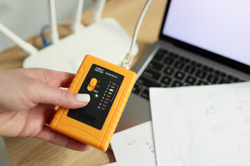 Woman holds LAN speed tester near Wi-Fi router and laptop