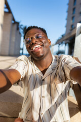 Happy young black man with glasses taking selfie looking at camera. Vertical image.