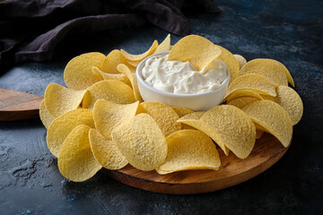 Close-up potato chips and sauce in a white bowl on a wooden cutting board.