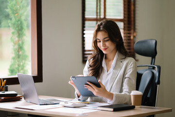 Asian businesswoman working in the office with working notepad, tablet and laptop documents .