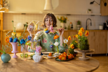 Young woman has a dinner with flowers, sitting by the table full of different flowers in vases and plate as a meal. Concept of beauty and flower diet