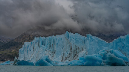Fototapeta na wymiar Amazing blue ice rises like a wall above the turquoise lake. Cracks on the surface. The mountains are hidden in rain clouds and fog. Perito Moreno glacier. Argentina. El Calafate. Lago Argentino