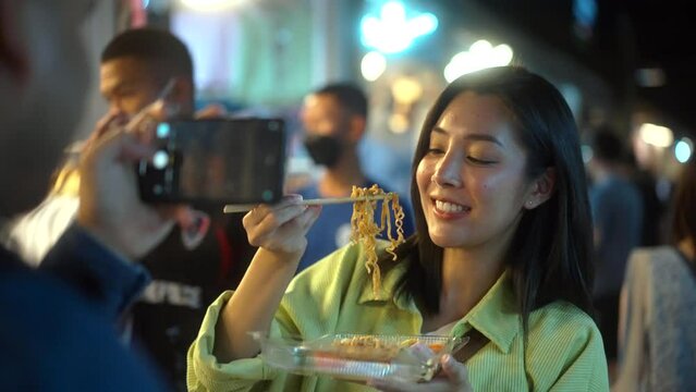 Solo traveler asian women enjoy buying and eating traditional street food night market take photo upload social media. Beautiful Tourists woman feeling happy buying street food in the evening.