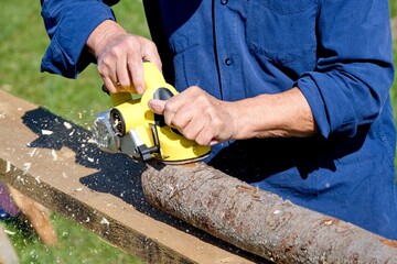 electric planer in the process of processing a whole dried log at a carpenter's workplace, cutting off the top texture and remaining bark from a long log, wood processing