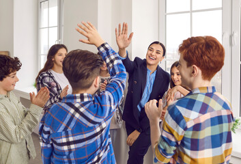 Group of children and their teacher having fun in the classroom. Happy woman teacher gives a high five to a student boy while others are clapping their hands. Support and teamwork at school concept