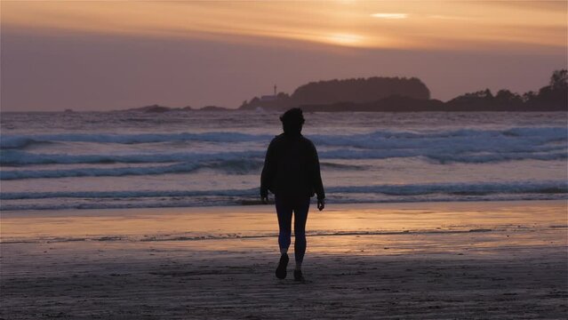 Adventurous Woman Standing on the Sandy Beach on the West Coast of Pacific Ocean. Cox Bay in Tofino, Vancouver Island, BC, Canada. Adventure Travel. Slow Motion