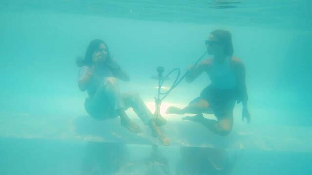 two girls pretend to smoke hookah at the bottom of the pool