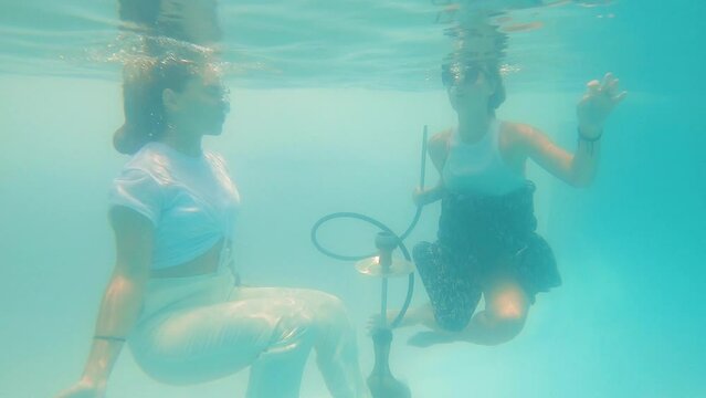 two girls pretend to smoke hookah at the bottom of the pool