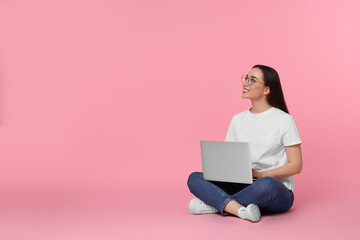 Fototapeta na wymiar Smiling young woman with laptop on pink background, space for text