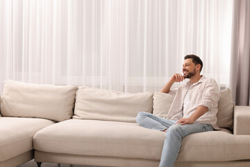 Fototapeta premium Happy man on resting sofa near window with beautiful curtains in living room. Space for text