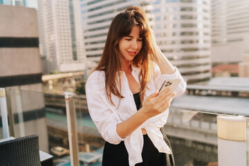 Fototapeta premium Pretty brunette woman using mobyle phone while walking in Bangkok. Modern architecture on background.