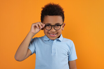 Cute African-American boy with glasses on orange background