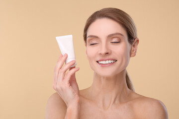 Woman holding tube of foundation on beige background