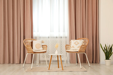 Living room with pastel window curtains, wooden table and rattan chairs