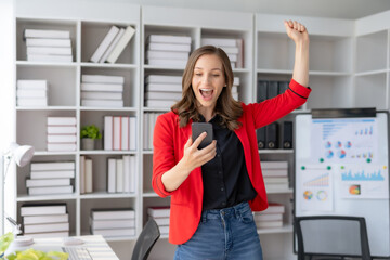 Happy businesswoman raising hands with victory smiling happily with smart phone. The concept of success at work.