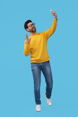 Smiling man taking selfie with smartphone on light blue background