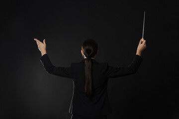 Professional conductor with baton on dark background, back view