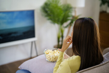 Asian woman Watching smart TV and using remote controller Hand holding television audio remote control at home with the remote control television