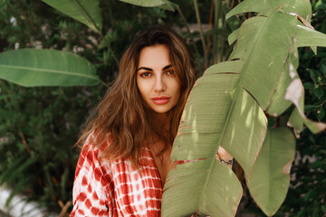 Young woman's face surrounded by tropical leaves. Closeup portrait of magnificent lady with natural nude makeup, perfect skin, wavy  hair. Natural cosmetic, wellness, purity, skincare, .beauty concept