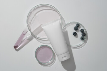 Cleansing and moisturizing tube cosmetics on white background with lab glassware, fresh blueberries and essence. Scene for advertising, space for design. Minimal style