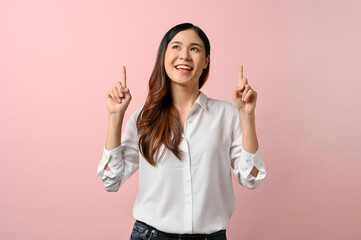 Pretty young woman pointing above her head while standing on pink isolated background.