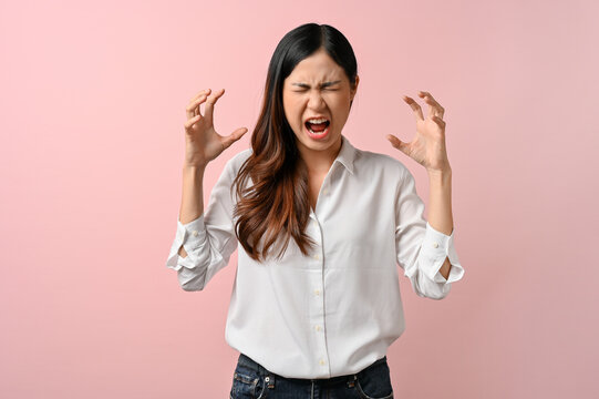 Upset Asian woman having a headache on pink isolated background.