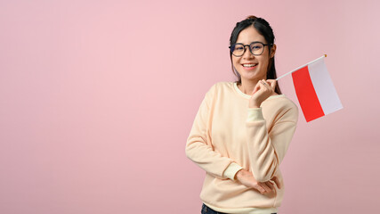 Cheerful young Asian woman showing a Poland flag on pink isolated background
