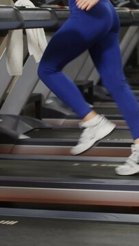 Young beautiful woman in sportswear runs on a treadmill doing in the gym, close-up with a gradual shift video from women's legs to the woman's face