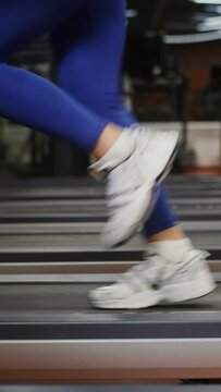 Close-up video footage of indoor gym. Women's legs in sports stylish shoes running fast on a treadmill, unrecognizable personality, no face
