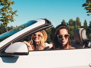 Portrait of two young beautiful and smiling hipster female in convertible car. Sexy carefree women...